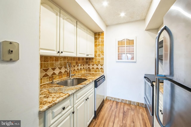 kitchen with appliances with stainless steel finishes, light wood-type flooring, white cabinets, light stone counters, and sink