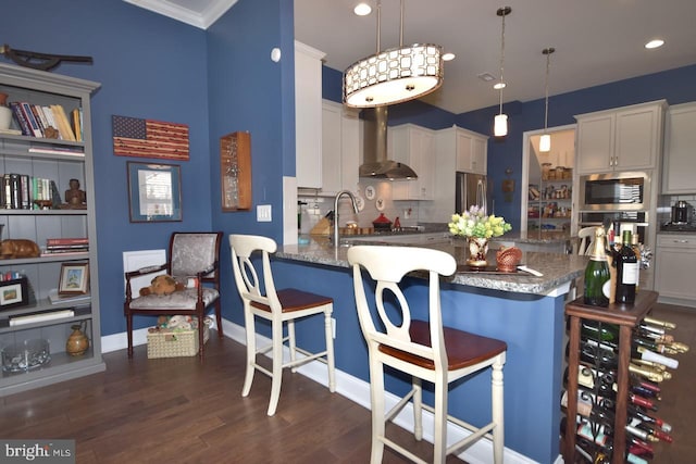 kitchen featuring stainless steel appliances, a breakfast bar area, hanging light fixtures, and wall chimney exhaust hood