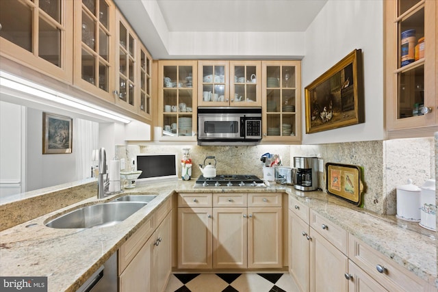 kitchen with appliances with stainless steel finishes, light brown cabinetry, tasteful backsplash, sink, and light stone countertops