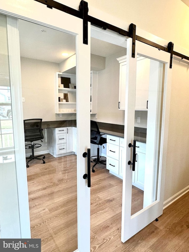 home office featuring built in desk, light wood-type flooring, and a barn door