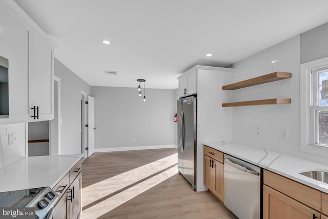 kitchen with light stone countertops, white cabinetry, appliances with stainless steel finishes, and light hardwood / wood-style flooring