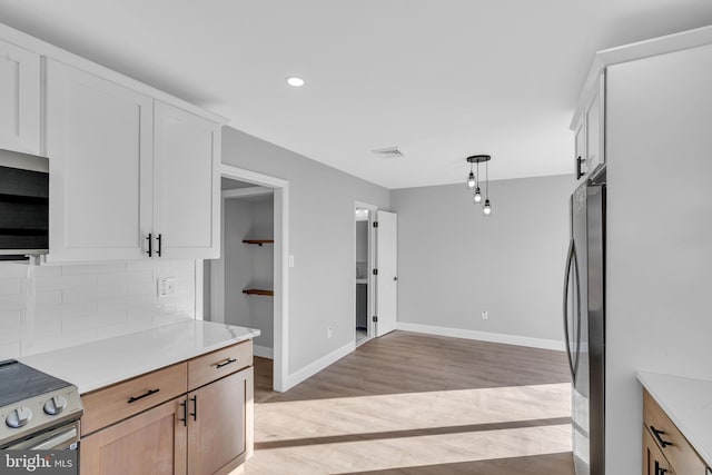 kitchen with appliances with stainless steel finishes, white cabinetry, decorative backsplash, light brown cabinets, and light hardwood / wood-style flooring