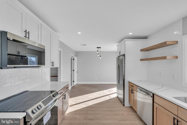 kitchen featuring appliances with stainless steel finishes, white cabinetry, backsplash, light stone countertops, and light wood-type flooring