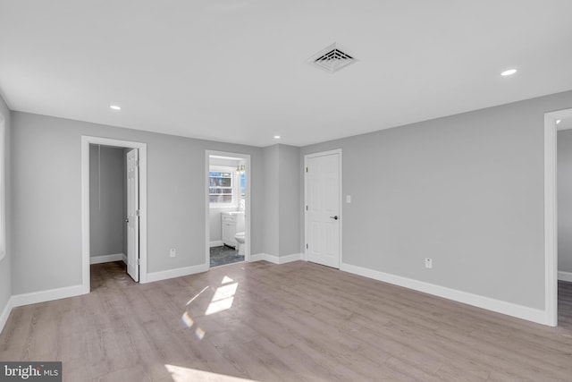 unfurnished bedroom with a closet, a walk in closet, ensuite bath, and light hardwood / wood-style flooring