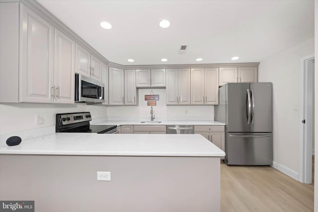 kitchen with sink, kitchen peninsula, stainless steel appliances, and light wood-type flooring