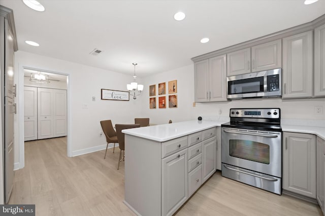 kitchen with kitchen peninsula, stainless steel appliances, gray cabinetry, a notable chandelier, and hanging light fixtures