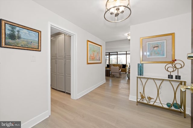 corridor with light hardwood / wood-style flooring and a notable chandelier