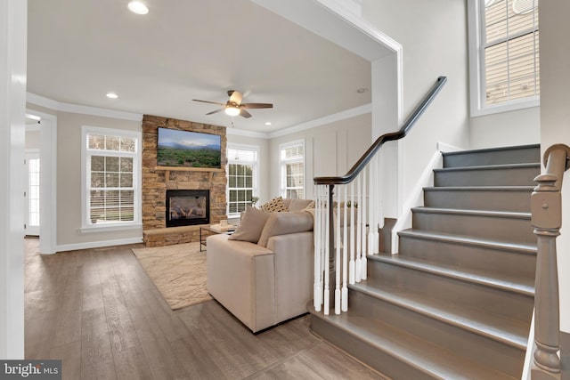 living room featuring ceiling fan, light hardwood / wood-style floors, a stone fireplace, and crown molding