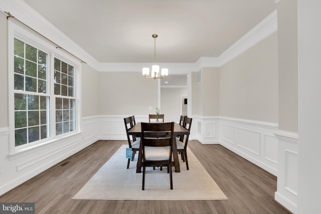 dining space featuring wood-type flooring, a notable chandelier, and crown molding