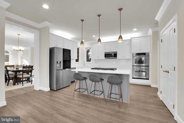 kitchen with an inviting chandelier, appliances with stainless steel finishes, a center island, white cabinetry, and decorative light fixtures