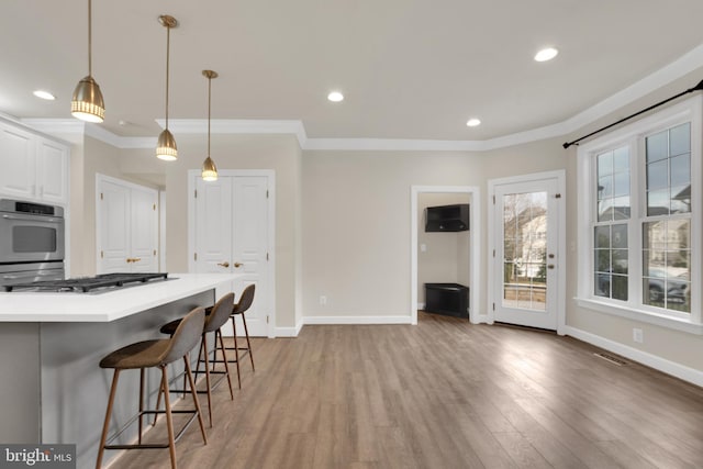 kitchen with a kitchen breakfast bar, appliances with stainless steel finishes, pendant lighting, hardwood / wood-style flooring, and white cabinets