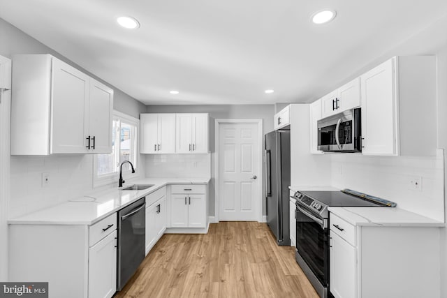 kitchen with tasteful backsplash, white cabinetry, sink, light hardwood / wood-style flooring, and stainless steel appliances