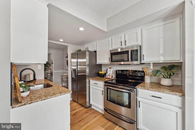 kitchen featuring white cabinetry, appliances with stainless steel finishes, tasteful backsplash, light stone counters, and sink