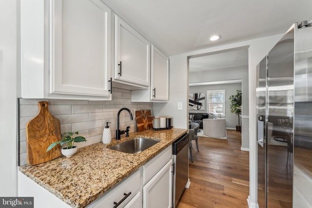 kitchen with appliances with stainless steel finishes, wood-type flooring, light stone countertops, white cabinets, and sink