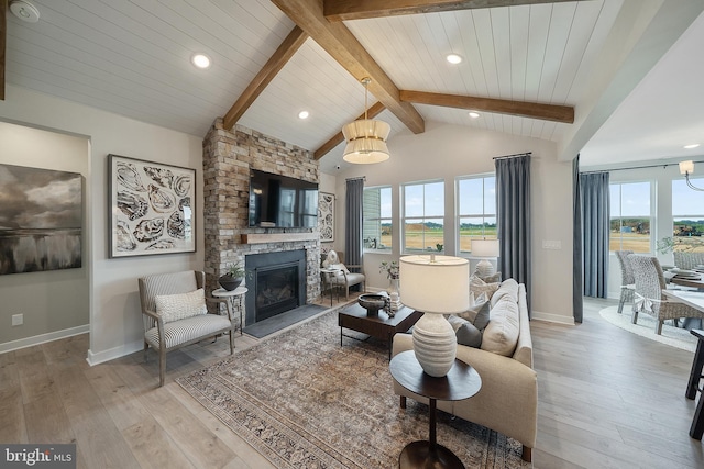 living room with a healthy amount of sunlight, vaulted ceiling with beams, light hardwood / wood-style flooring, and a stone fireplace