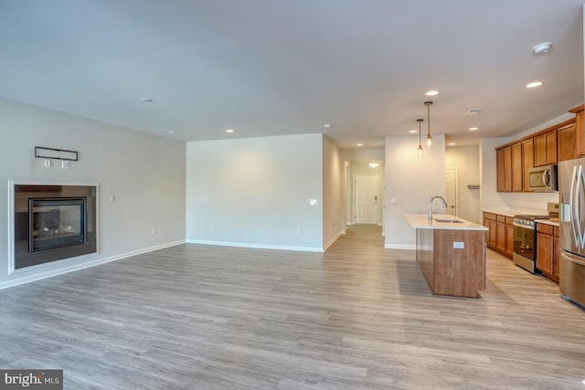 kitchen with decorative light fixtures, a center island with sink, sink, light hardwood / wood-style flooring, and appliances with stainless steel finishes