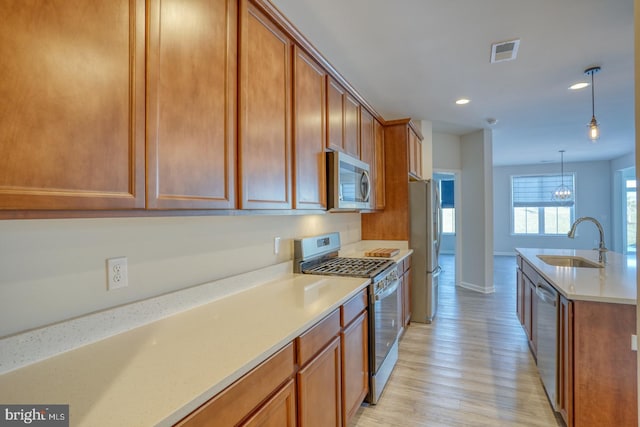 kitchen featuring decorative light fixtures, appliances with stainless steel finishes, sink, and light hardwood / wood-style flooring