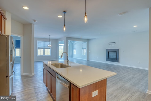 kitchen featuring light hardwood / wood-style floors, appliances with stainless steel finishes, a kitchen island with sink, hanging light fixtures, and sink