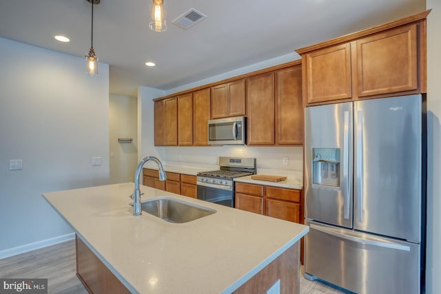 kitchen featuring sink, hanging light fixtures, a kitchen island with sink, light wood-type flooring, and stainless steel appliances