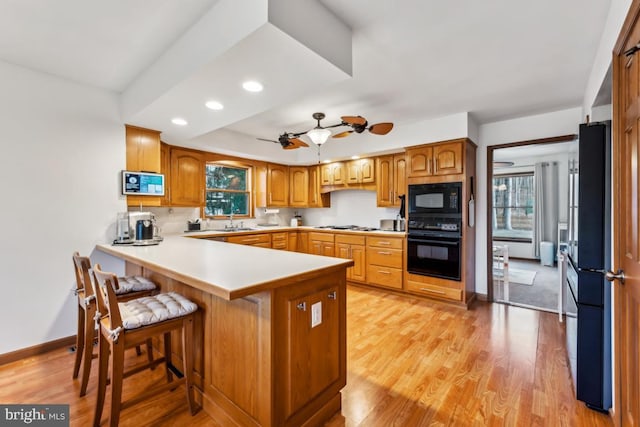 kitchen with kitchen peninsula, a breakfast bar, black appliances, tasteful backsplash, and light wood-type flooring