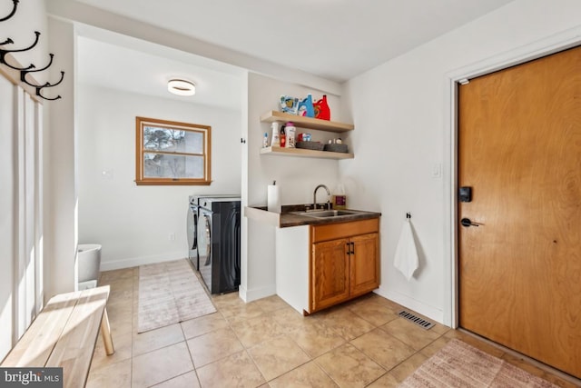 clothes washing area featuring separate washer and dryer, cabinets, sink, and light tile patterned floors