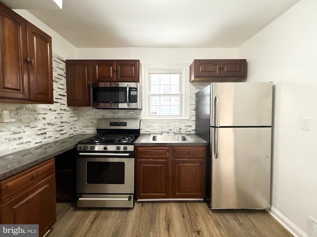 kitchen with sink, stainless steel appliances, hardwood / wood-style floors, and backsplash