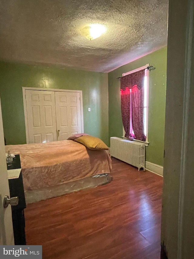 bedroom featuring a textured ceiling, a closet, radiator heating unit, and hardwood / wood-style floors