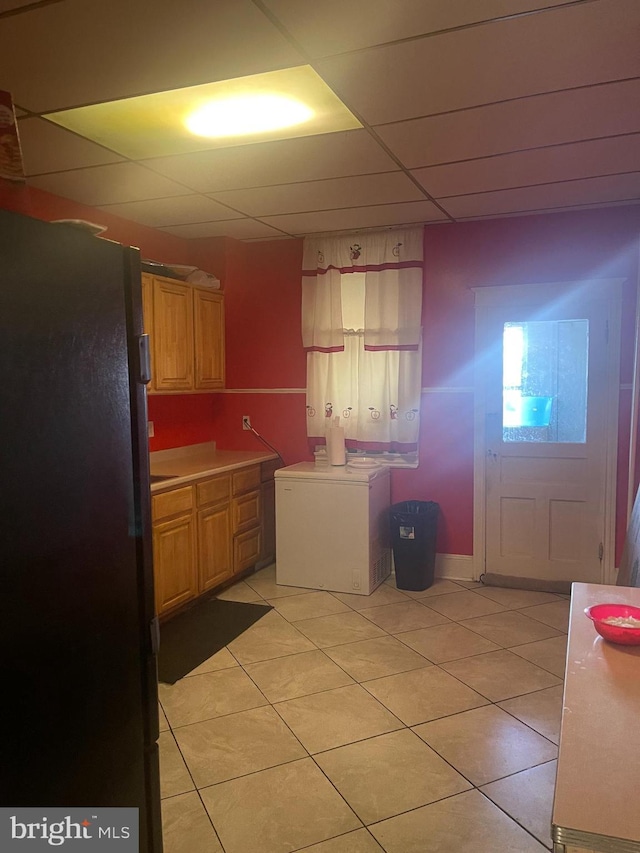 kitchen with a paneled ceiling, fridge, black refrigerator, and light tile patterned floors