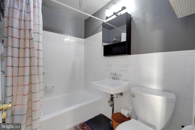 bathroom featuring tile walls, shower / bath combo with shower curtain, and toilet