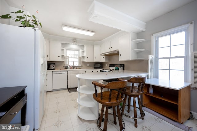 kitchen featuring white appliances, kitchen peninsula, white cabinets, and a kitchen bar