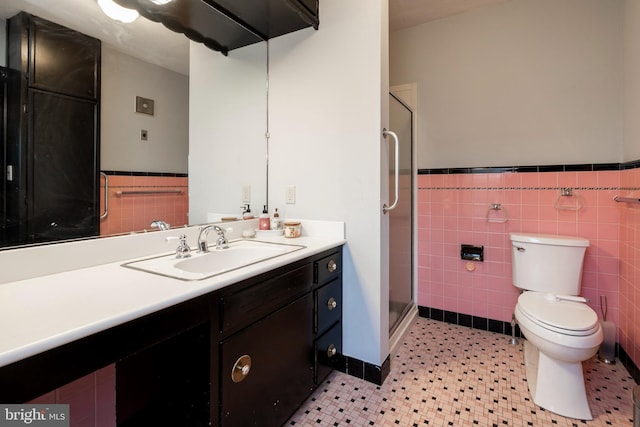 bathroom with toilet, vanity, tile patterned floors, tile walls, and a shower with shower door