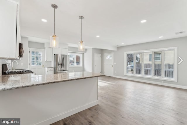 kitchen featuring light stone countertops, white cabinets, pendant lighting, and stainless steel fridge