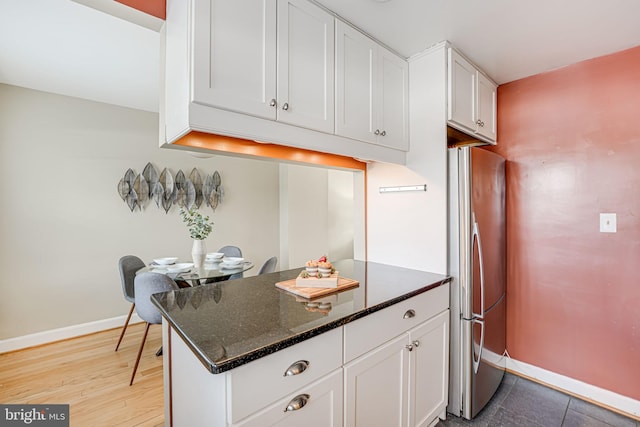 kitchen featuring white cabinets, stainless steel fridge, dark stone counters, and light wood-type flooring