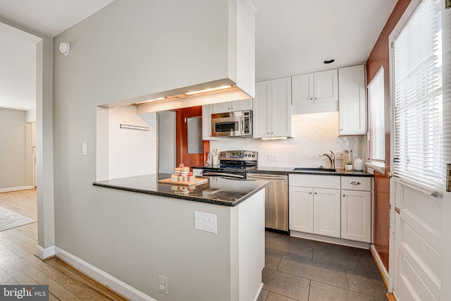 kitchen with appliances with stainless steel finishes, white cabinetry, sink, dark stone countertops, and kitchen peninsula