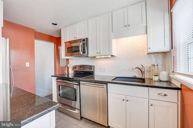 kitchen featuring white cabinetry, sink, dark stone countertops, stainless steel appliances, and light tile patterned flooring