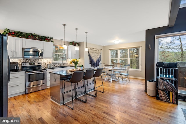 kitchen featuring stainless steel appliances, white cabinets, decorative light fixtures, a kitchen breakfast bar, and a kitchen island