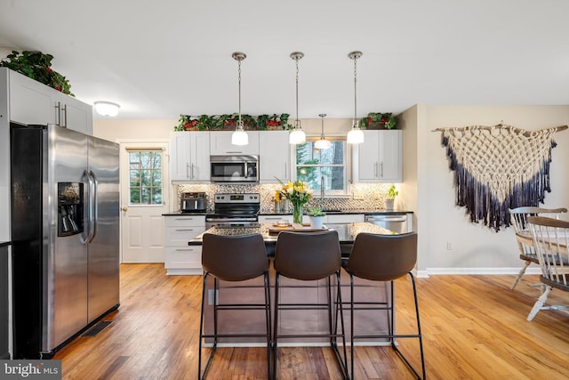 kitchen with white cabinetry, stainless steel appliances, hanging light fixtures, light hardwood / wood-style flooring, and tasteful backsplash