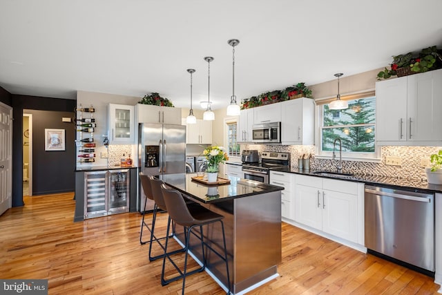 kitchen with stainless steel appliances, sink, white cabinetry, a kitchen island, and wine cooler