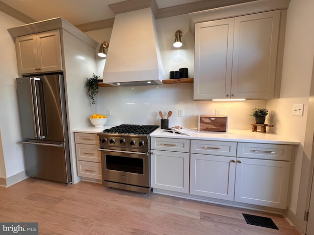 kitchen featuring premium range hood, backsplash, high end appliances, ornamental molding, and light wood-type flooring