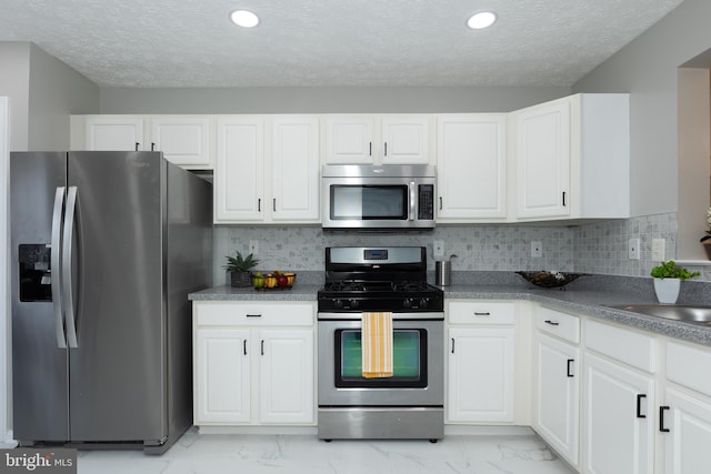 kitchen with a textured ceiling, white cabinetry, tasteful backsplash, and appliances with stainless steel finishes