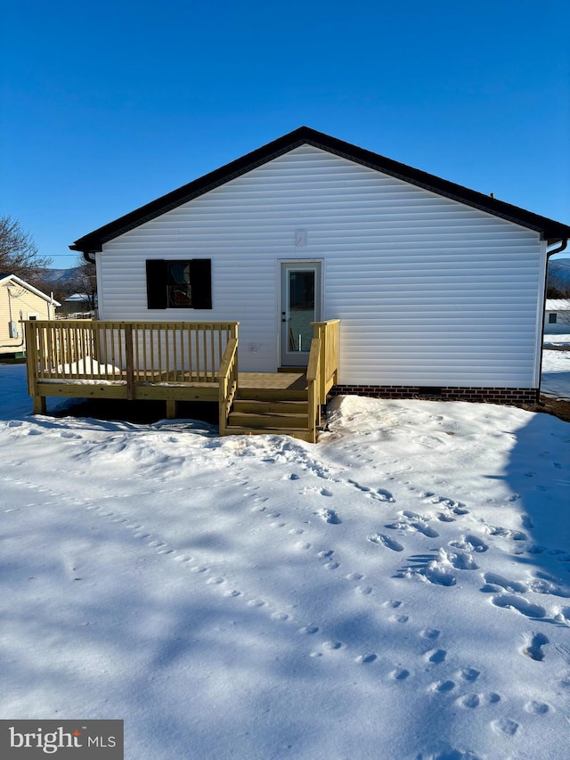 snow covered back of property with a deck