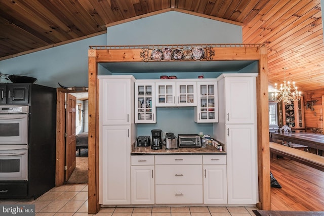 kitchen with lofted ceiling, double oven, white cabinets, and wooden walls