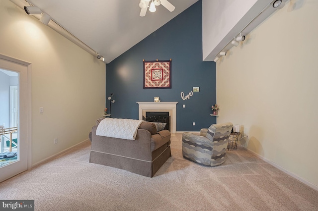 living area with baseboards, a glass covered fireplace, carpet, high vaulted ceiling, and track lighting