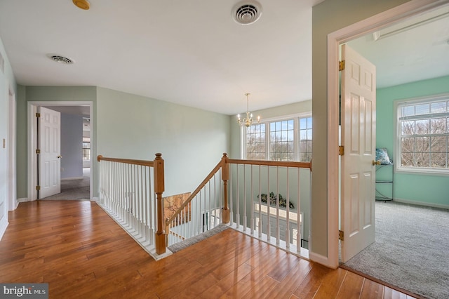 corridor with an inviting chandelier, visible vents, hardwood / wood-style floors, and an upstairs landing