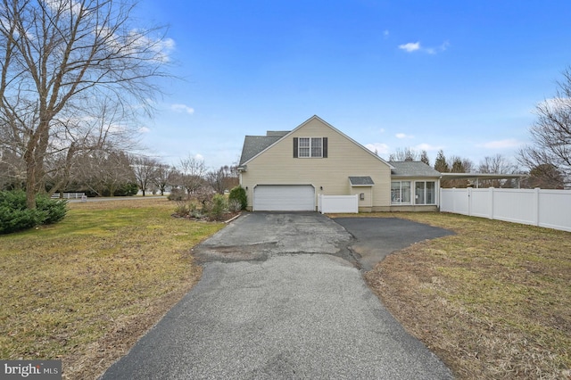 traditional-style home with a garage, a front lawn, fence, and aphalt driveway