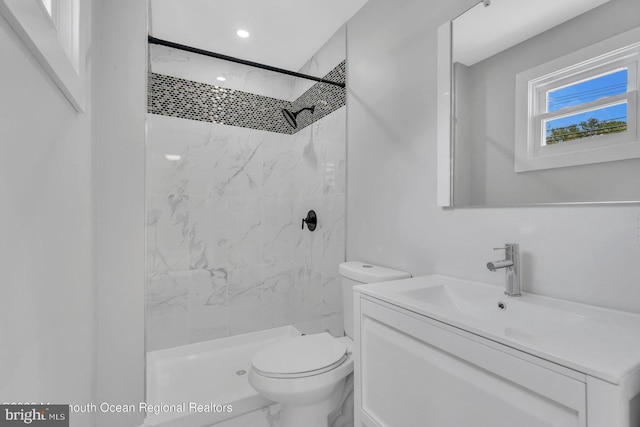 bathroom featuring toilet, tiled shower, and vanity