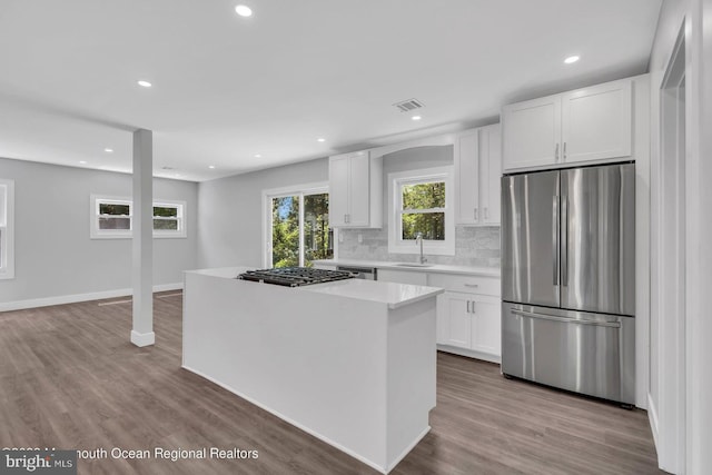 kitchen featuring stainless steel appliances, a healthy amount of sunlight, a kitchen island, white cabinetry, and backsplash