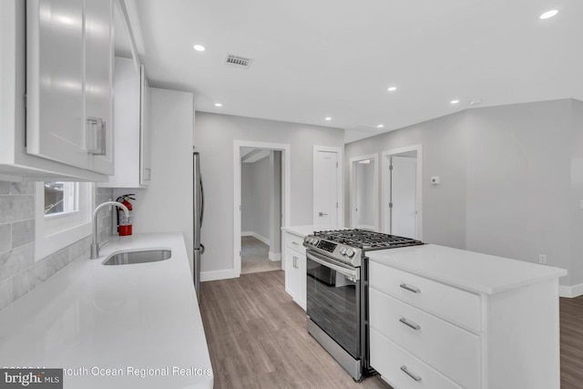 kitchen with stainless steel appliances, white cabinetry, sink, and light hardwood / wood-style floors