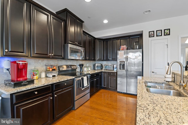 kitchen with sink, stainless steel appliances, light hardwood / wood-style floors, and light stone countertops