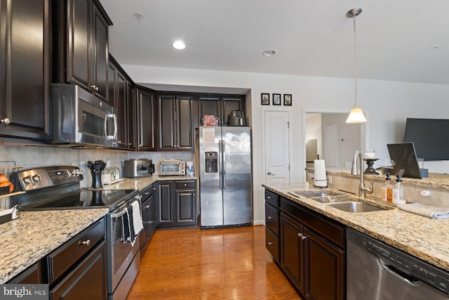 kitchen with dark brown cabinets, pendant lighting, sink, light stone countertops, and stainless steel appliances